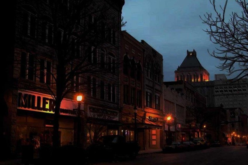 Una escena nocturna en la calle con edificios iluminados y una torre de reloj destacada. 1