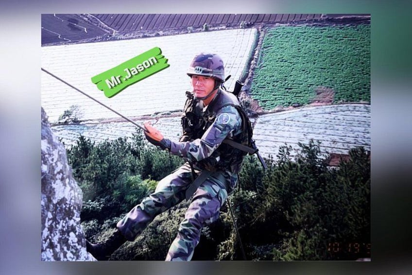 A person in military attire rappelling down a rocky surface with a green sign reading 'Mr. Jason'. 3