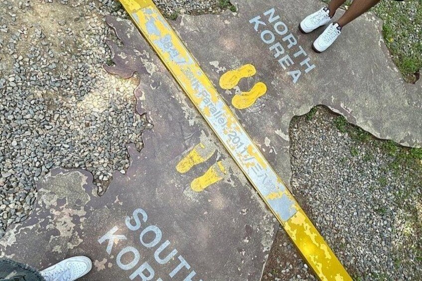 A road with a yellow line and text indicating a border between North Korea and South Korea. 3