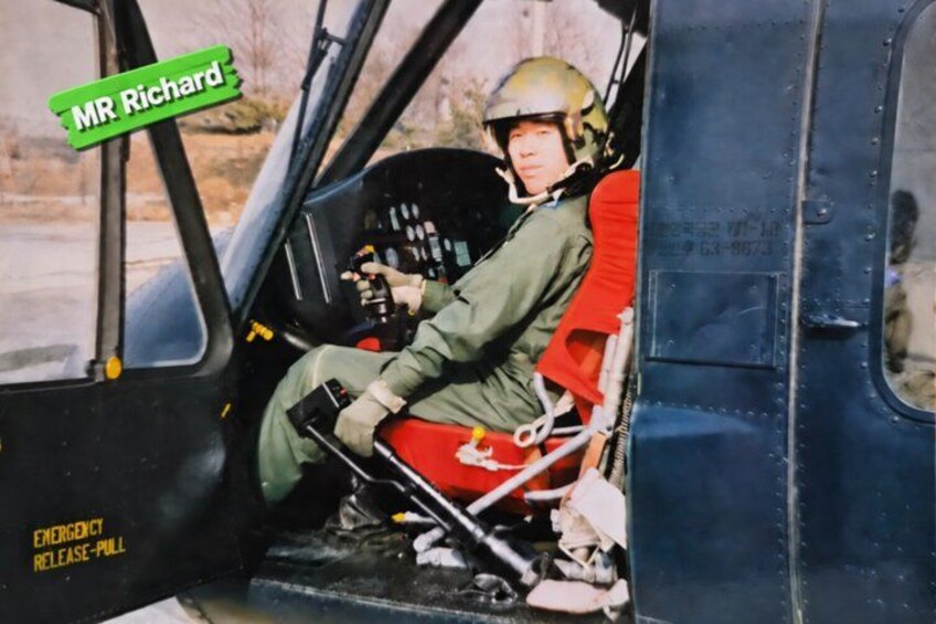Een persoon in de cockpit van een helikopter, draagt een helm en een groene jas. 4