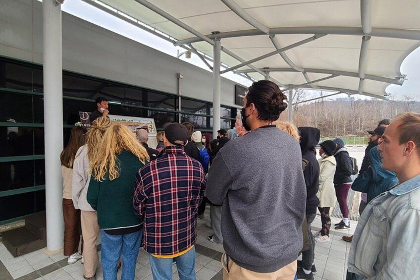 A group of people standing in a covered outdoor area with a building entrance. 2