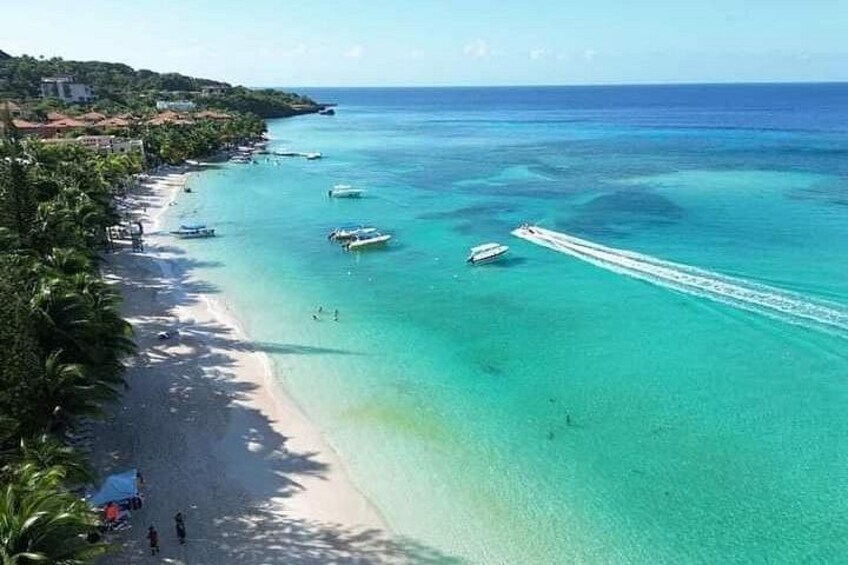 A beach with clear turquoise water, a few boats, and a few people walking along the shore. 5