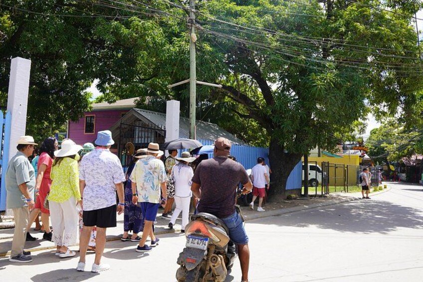 A group of people standing on a street, a motorcycle, and a blue fence. 2
