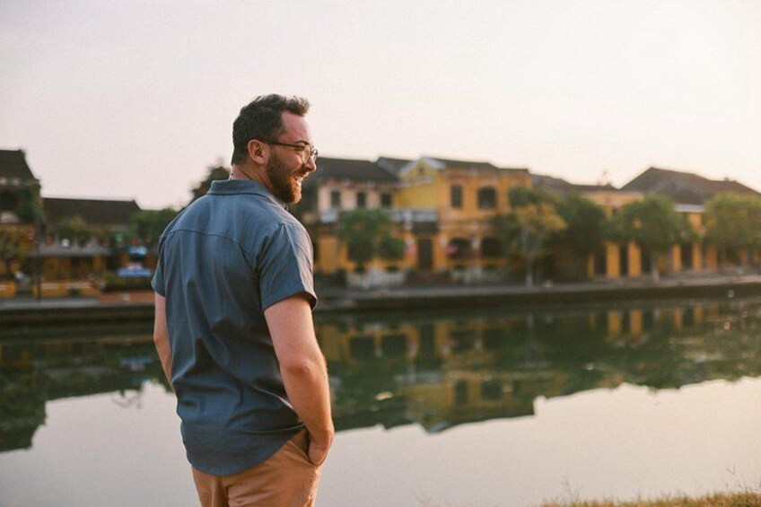 A man standing by a calm body of water with buildings in the background. 3
