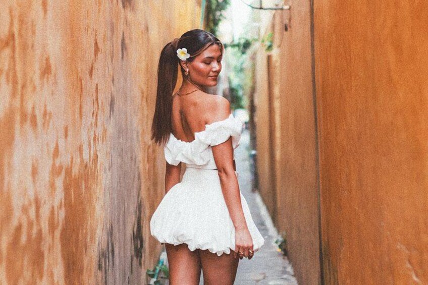 A person in a white dress walking down a narrow alleyway with textured walls. 2