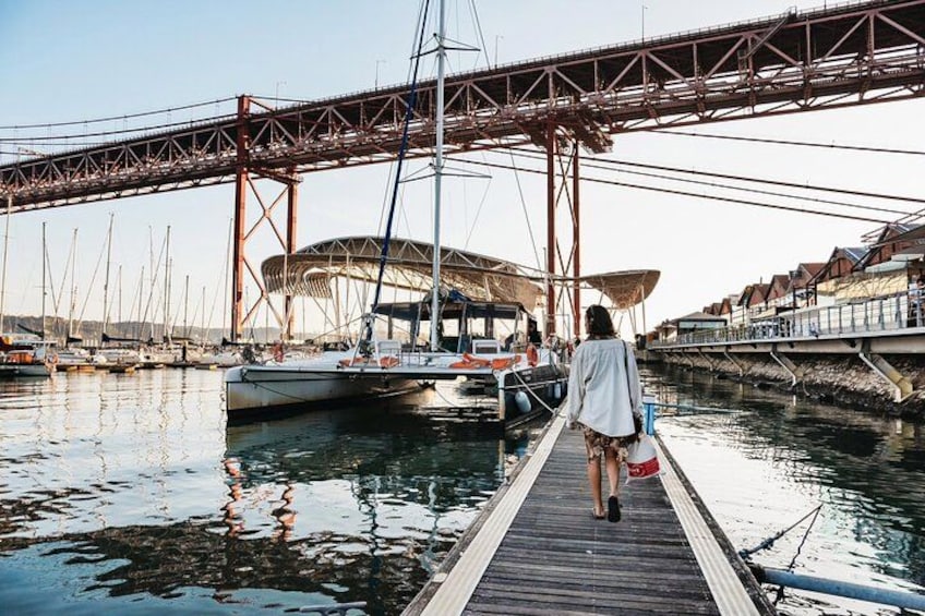 A person walking on a wooden dock towards a boat, a bridge, and a stadium in the background. 1