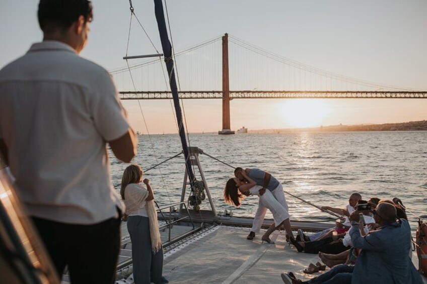 A sailboat with people on deck, a bridge in the background, and a sunset. 4