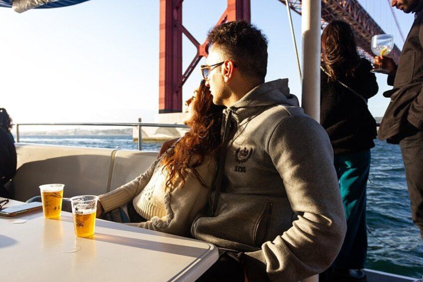 A person sitting at a table with drinks, a bridge in the background, and a body of water. 4