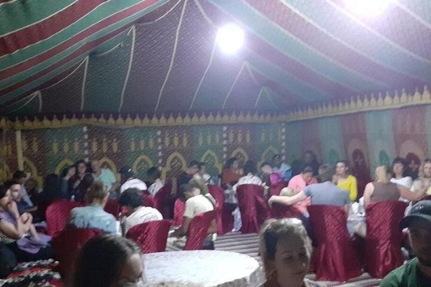 Un gruppo di persone riunite in un'area coperta da una tenda, con un muro decorato e un soffitto rivestito di tessuto drappeggiato. 5