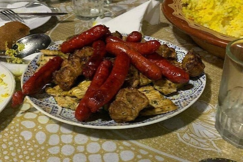 Un piatto con salsicce e carne, una ciotola di riso e un bicchiere d'acqua su un tavolo. 3