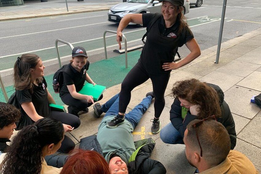 A group of people gathered around a person lying on the ground, possibly in a medical or training scenario. 5