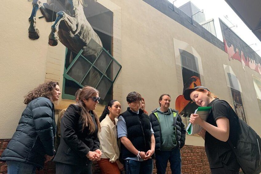 A group of people standing in front of a building with a mural of a horse. 3