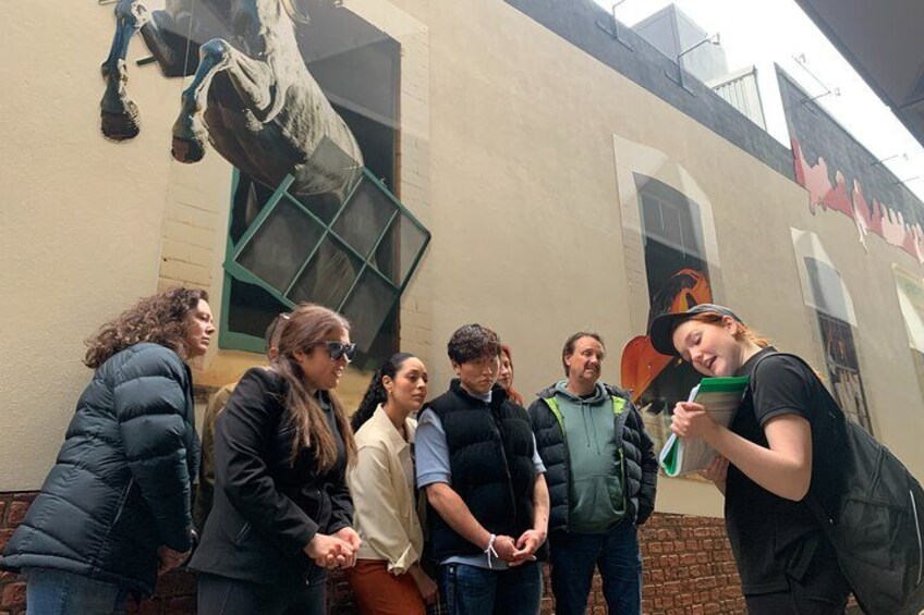 A group of people standing in front of a building with a mural of a horse. 2
