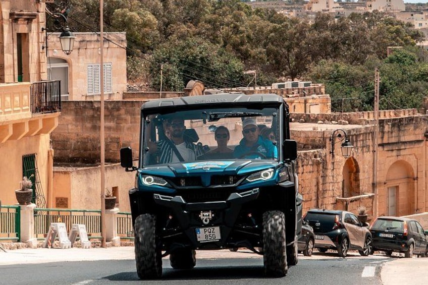 A black SUV driving on a road with buildings and trees in the background. 1