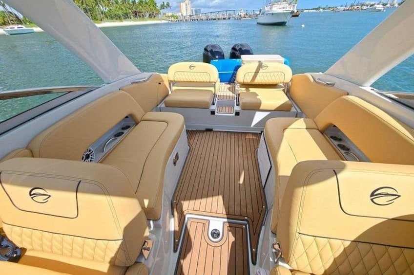 A boat deck with yellow leather seating, a central console, and a view of the water with other boats and a distant shoreline. 1