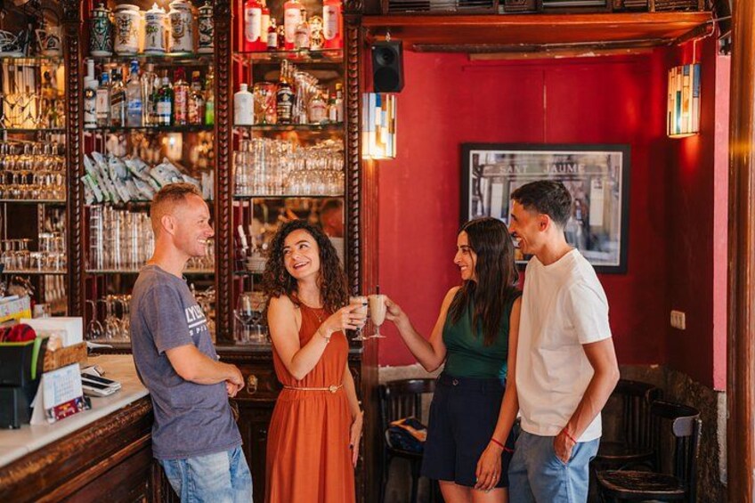 Un bar avec des étagères remplies de bouteilles et de verres, un mur rouge et un tableau encadré. 2