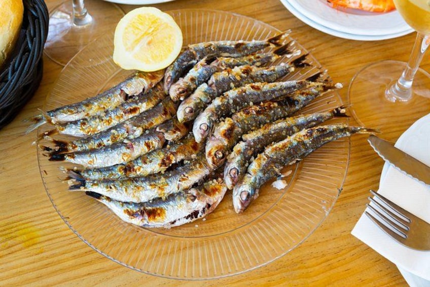 En tallerken med grillede sardiner, citronbåde og et glas hvidvin på et træbord. 4
