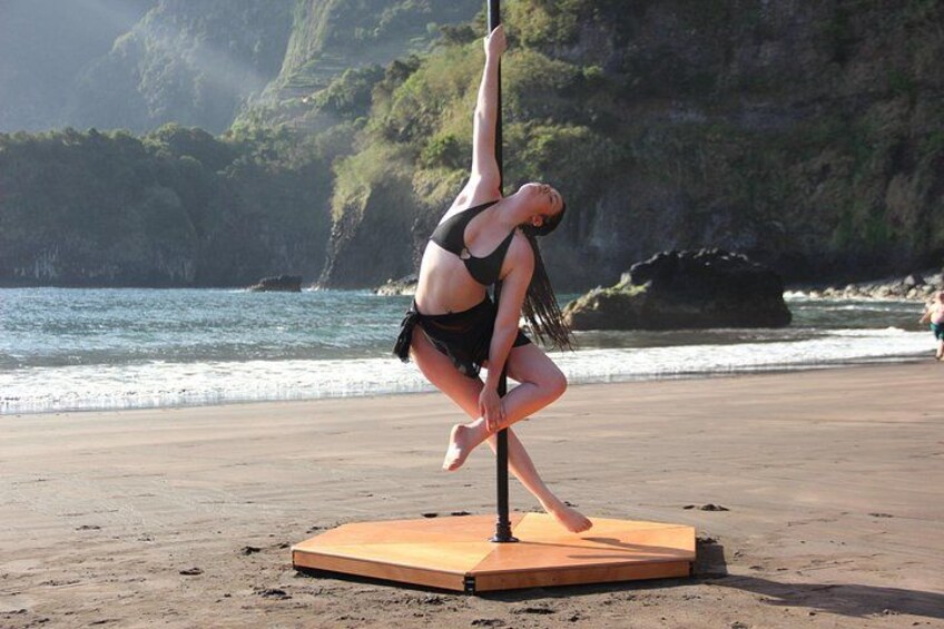 A person performing pole dancing on a mat at a beach with cliffs in the background. 1