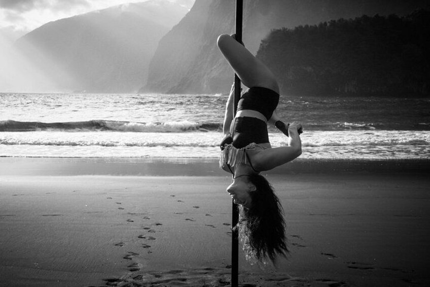 A person performing an aerial yoga pose on a pole by the ocean with mountains in the background. 5