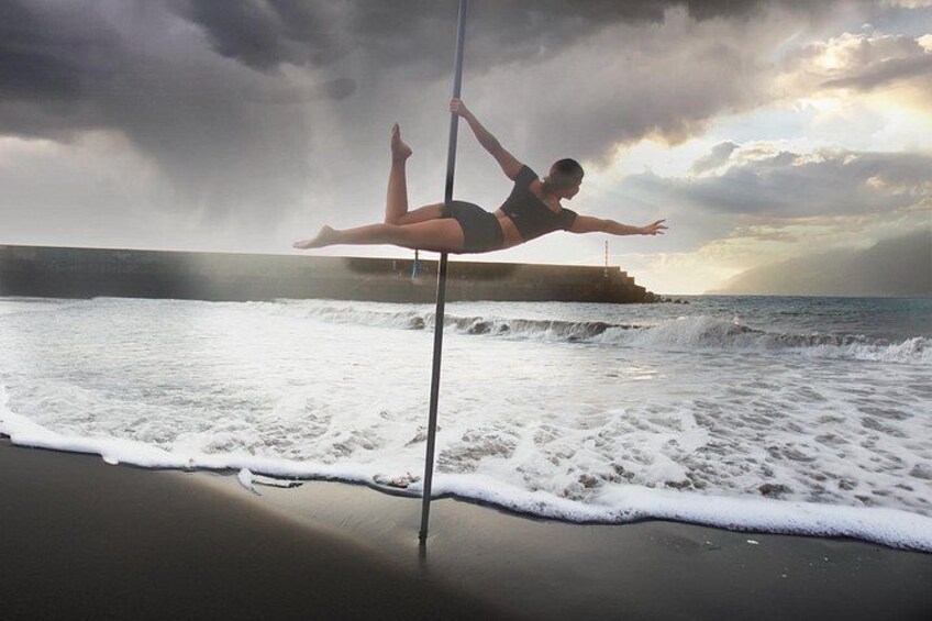 A person pole dancing on a beach with waves in the background. 3