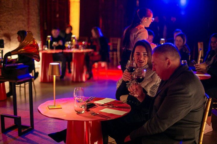Een sfeervol verlicht restaurant met ronde tafels, gasten die dineren, en een rode loper. 5