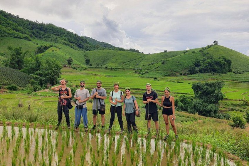 Un grupo de personas de pie en un campo de arroz con colinas verdes al fondo. 1