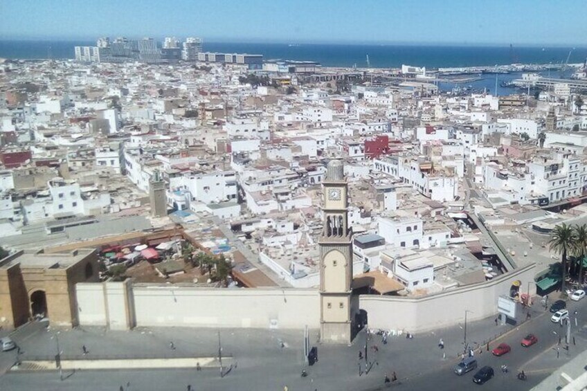 A coastal cityscape with a prominent clock tower, dense urban buildings, and a marina in the background. 3