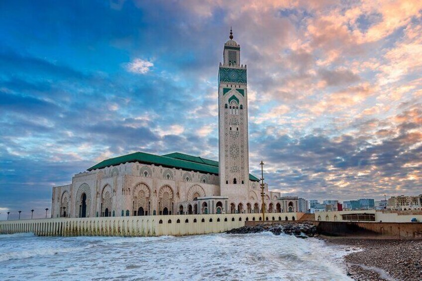 A mosque with a tall minaret and a green roof, situated by the sea. 1