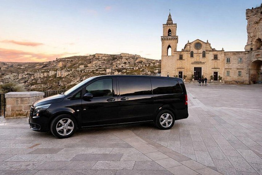 A black van parked in front of a historic building with a bell tower. 2