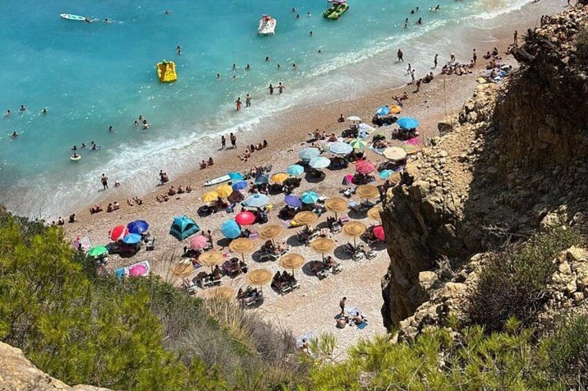 A crowded beach with people swimming and sunbathing under colorful umbrellas. 2