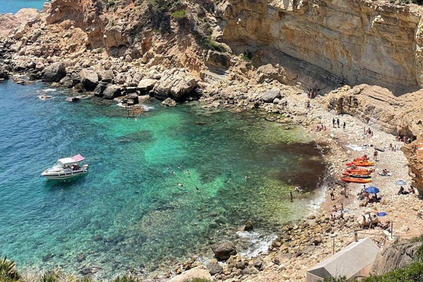 A rocky coastal area with clear turquoise water, a small boat, and people on the beach. 4