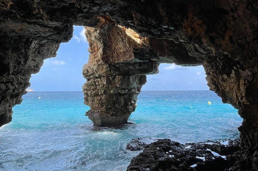 A natural rock formation with a cave entrance overlooking turquoise waters. 3