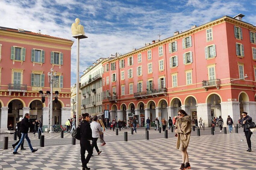 A public square with people walking, a statue, and classical architecture. 5