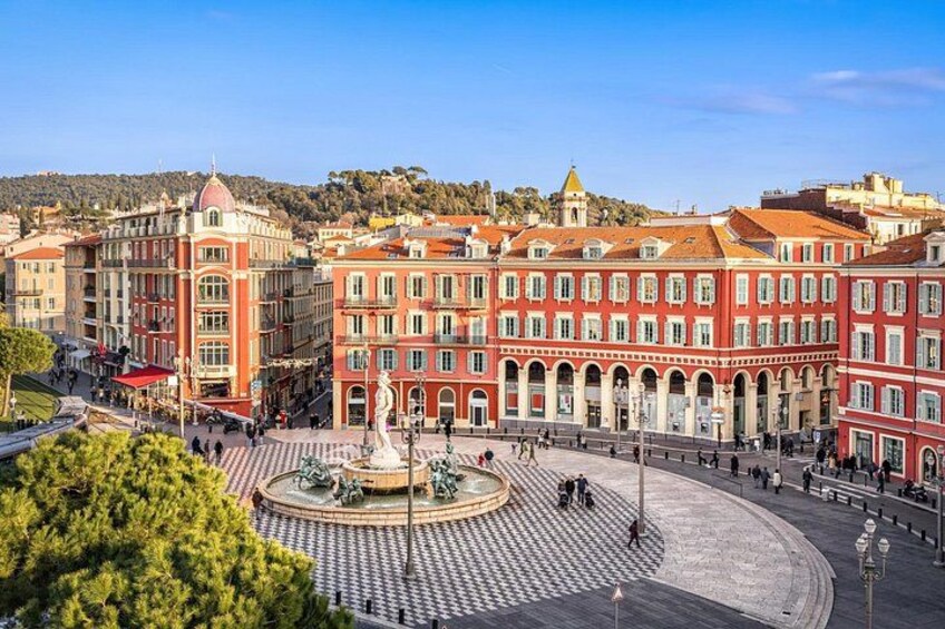 A plaza with a fountain, red buildings, and a hilly background. 3