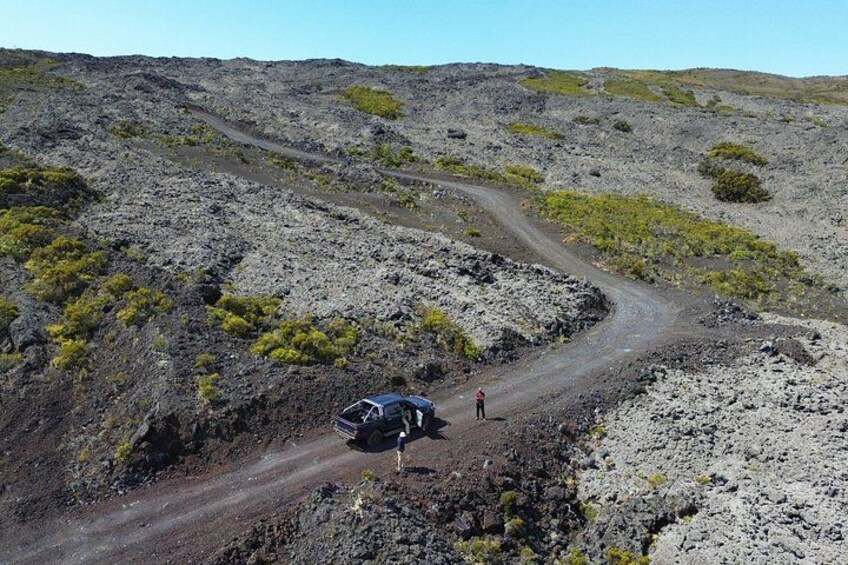 A rugged terrain with a winding dirt road, sparse vegetation, and a vehicle parked on the side. 1
