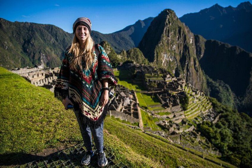 A person standing on a grassy slope with Machu Picchu ruins in the background. 2