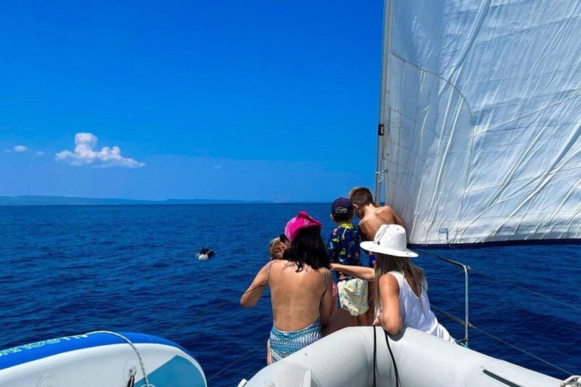 Een zeilboot met mensen aan boord, een heldere blauwe lucht en rustig zeewater. 1