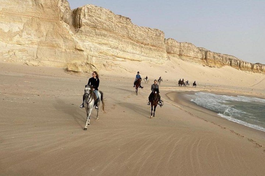 Des cavaliers sur une plage, avec des falaises en arrière-plan. 5