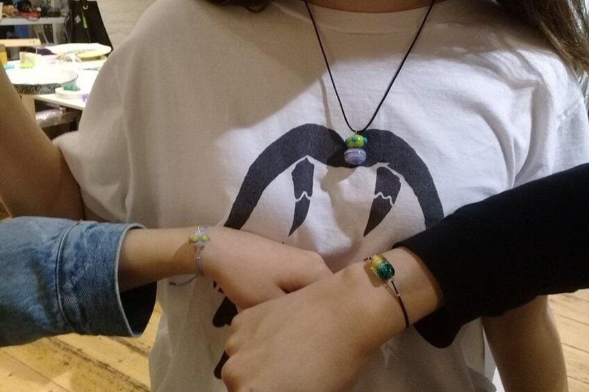 A person wearing a white t-shirt with a graphic design, holding a bracelet with a green stone. 5
