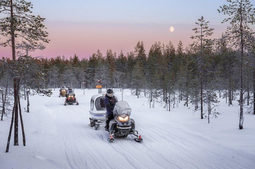 Sendero para motos de nieve en un área boscosa, cielo despejado y luna visible. 2