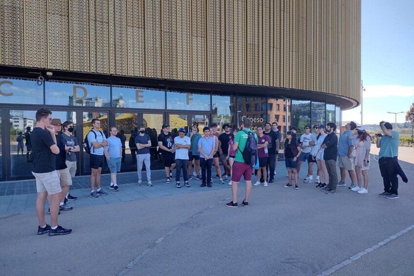 A group of people standing in front of a modern building with large glass windows. 1
