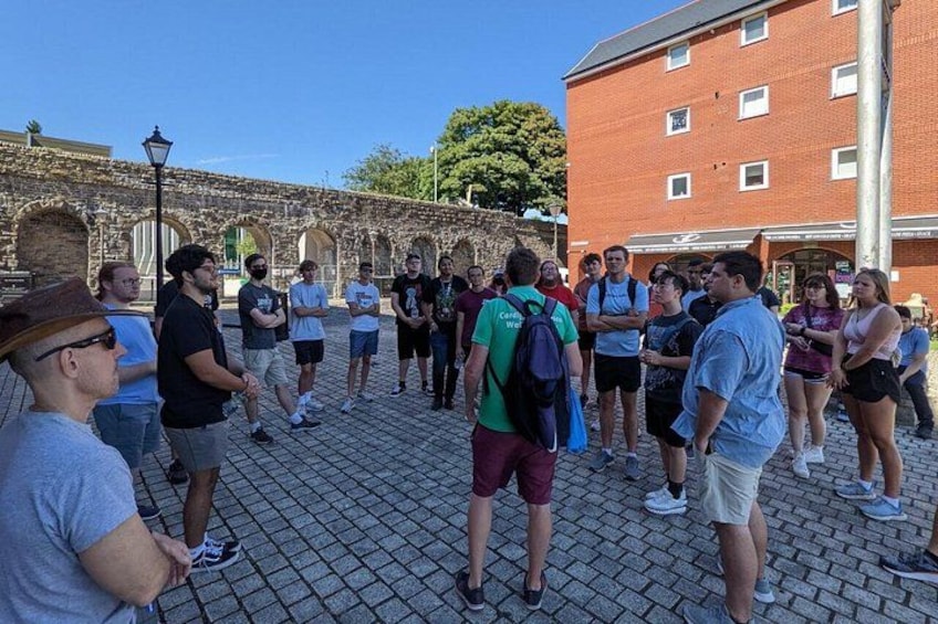 A group of people standing in a cobblestone courtyard with a historic stone wall and a red brick building in the background. 4