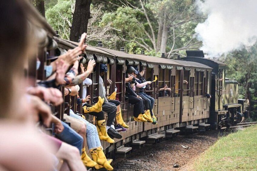A train with passengers wearing yellow boots and helmets, traveling on tracks surrounded by trees. 1