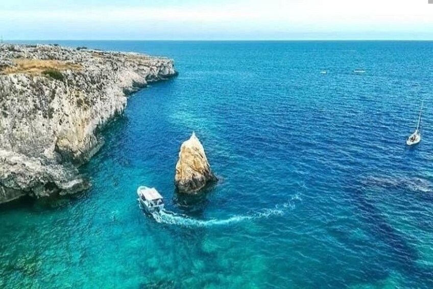 Un paysage côtier avec une falaise rocheuse, une mer bleue et limpide, et un voilier. 2