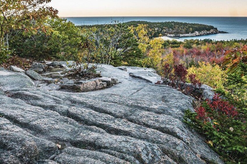 A rocky terrain with autumn foliage and a distant view of a coastline. 2