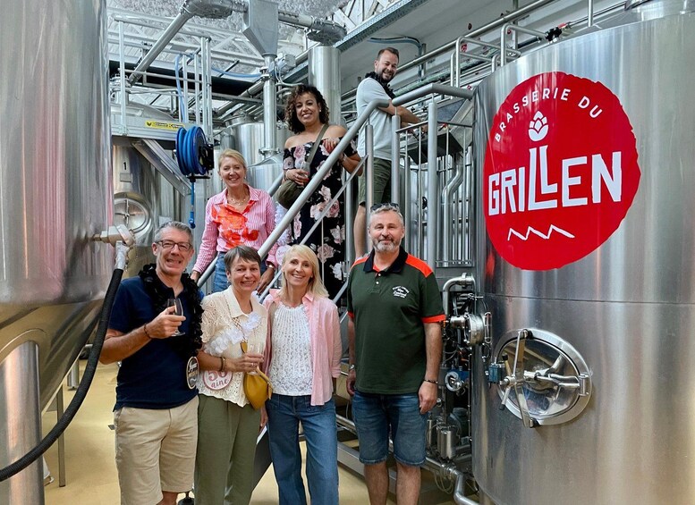 A group of people in a brewery setting with stainless steel tanks and a red sign that reads 'BRASSERIE DU GRILEN'. 4