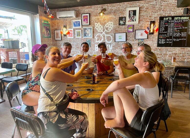 A group of people toasting with drinks around a wooden table in a brick-walled venue with posters on the wall. 3