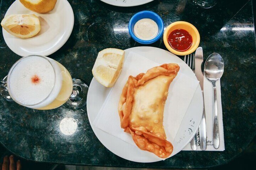 A plate with a pastry, lemon wedges, and two small bowls of sauce on a table. 1