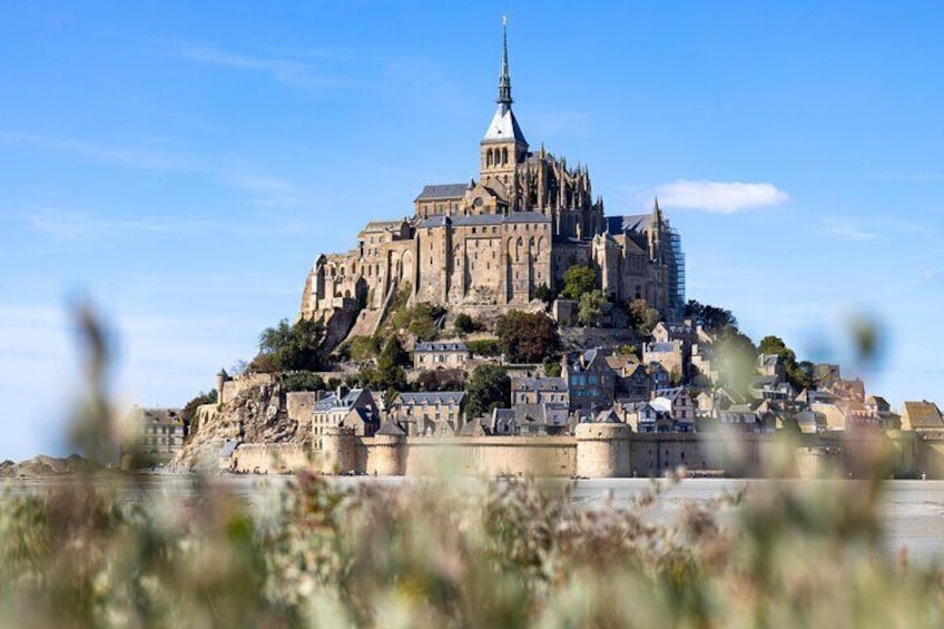 A historic castle on a hill with a prominent tower, surrounded by smaller buildings and a clear sky. 1