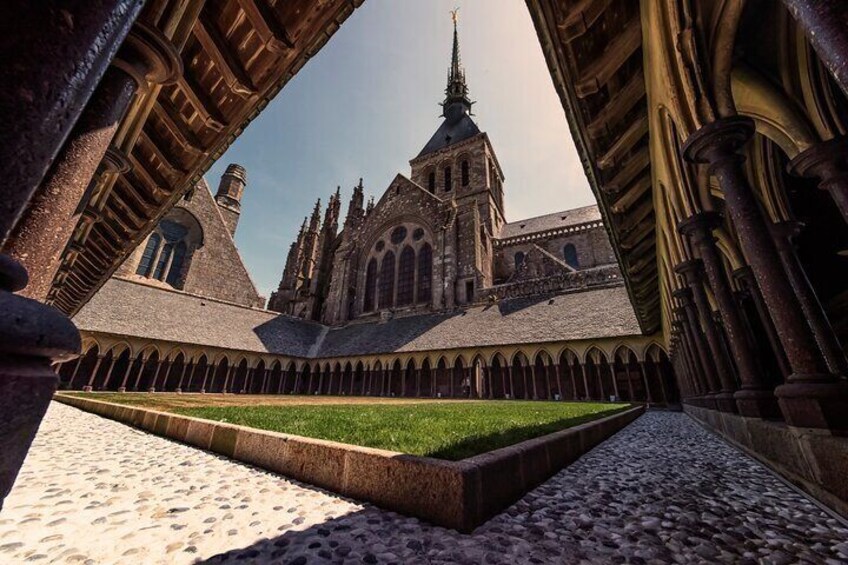 A medieval cloister with a central lawn, stone arches, and a prominent church tower. 2